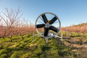 large industrial fan sits in a peach orchard, ready for frost and cold May temperatures